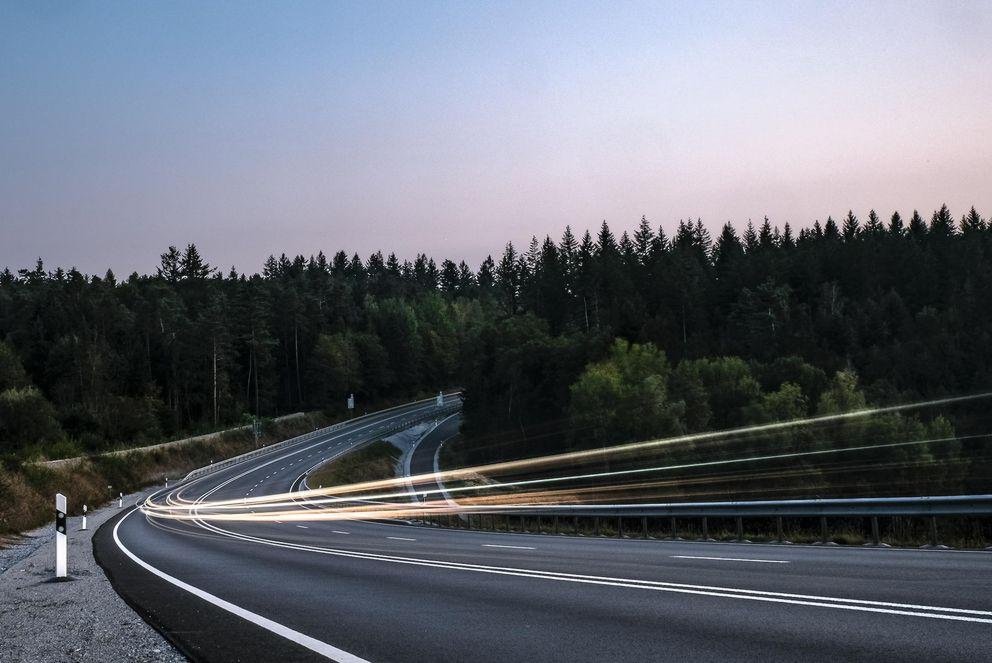 Lichter des Autoverkehrs auf einer Landstraße in der Abenddämmerung als Symbolbild für Mobilität im ländlichen Raum..