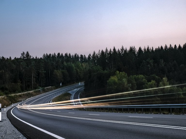 Lichter des Autoverkehrs auf einer Landstraße in der Abenddämmerung als Symbolbild für Mobilität im ländlichen Raum..