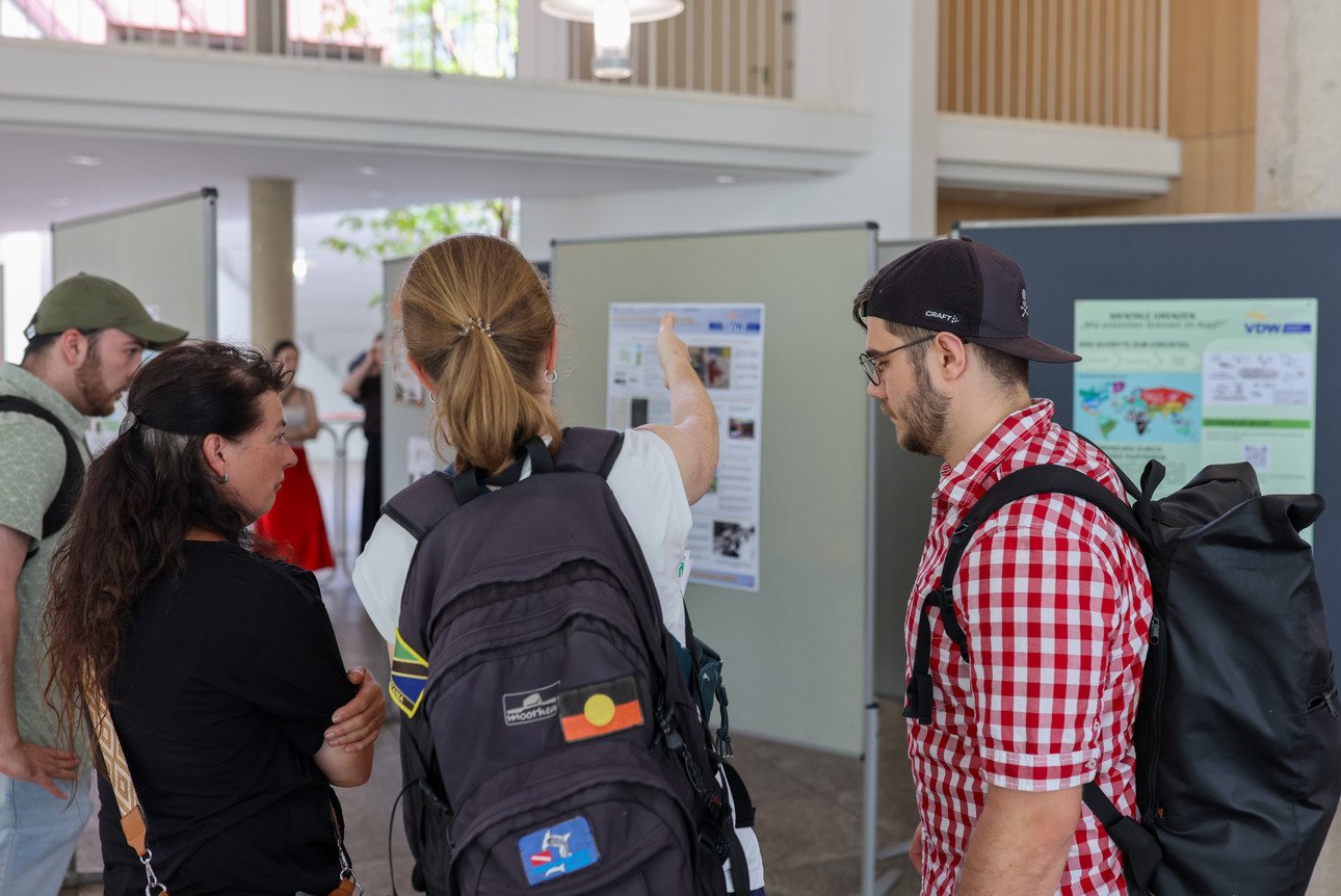 Im Foyer des Audimaxes der Universit&auml;t Passau blicken vier Studierende mit dem R&uuml;cken zur Kamera auf ausgestellte Poster der Seminarreihe "Grenzen &uuml;berwinden".