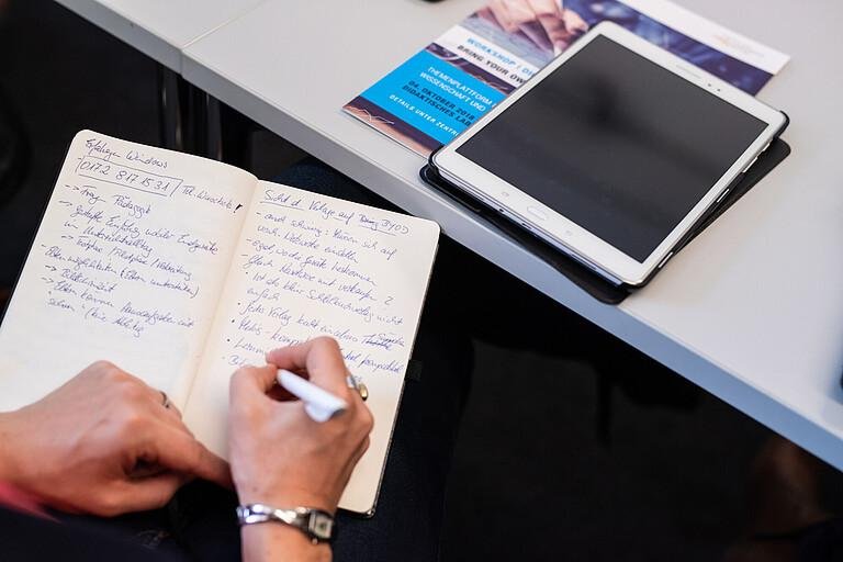 Person schreibt in Notizbuch auf dem Tisch ein Tablet