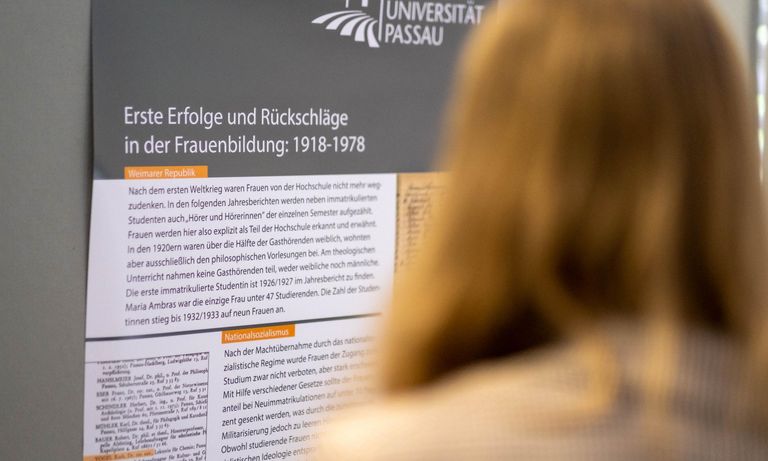 Frau steht vor Plakat zur Ausstellung „Akademische Bildung von Frauen in Passau 1622 bis 2022“