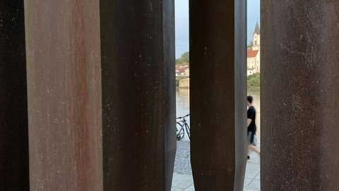 [Translate to Tschechisch:] Nahansicht durch die Skulptur hindurch, im Hintergrund jenseits des Inns zu sehen ist die Kirche St. Gertraud