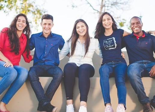 Fünf junge Menschen verschiedener Geschlechter und Herkunft sitzen lachend nebeneinander