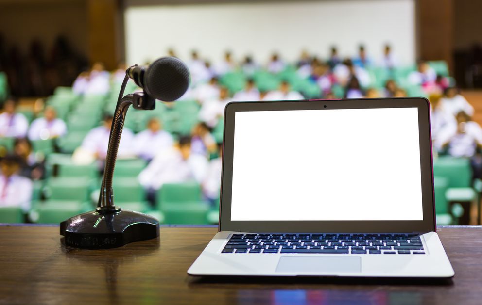 Podium mit Laptop und Mikrofon vor Publikum