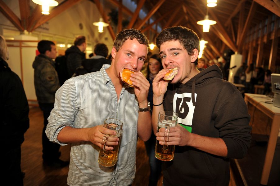 Zwei Studierende beißen in ein Leberkäs'-Brötchen mit einem Bierkrug in der Hand