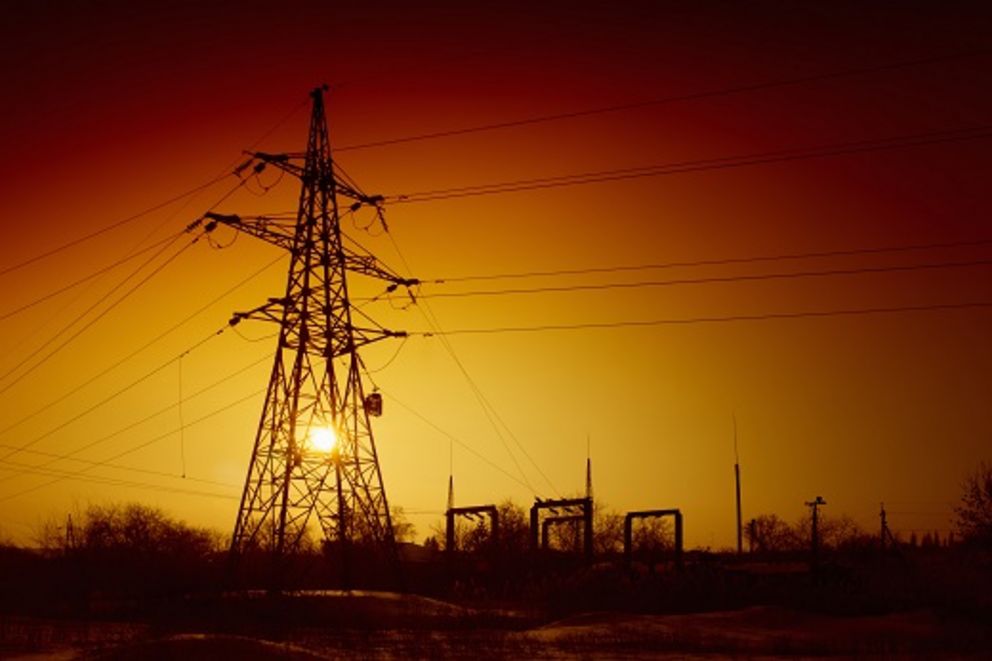 Foto eines schwarz erscheinenden Hochspannungsmast vor einem gelb-rot schimmerndem Himmel