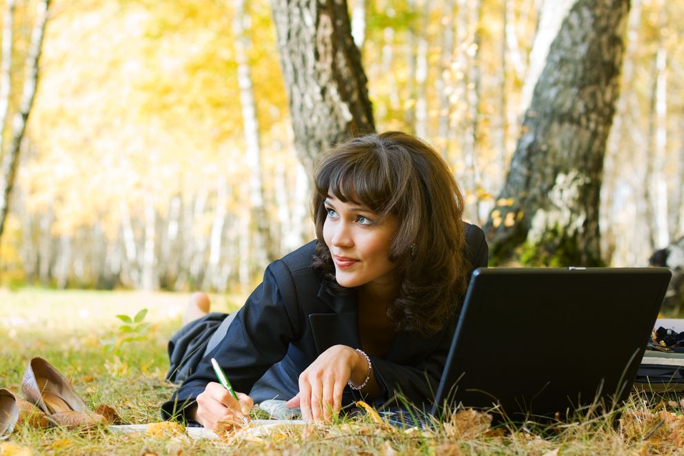 Unternehmerin liegt auf dem Boden in Birkenwald mit Laptop