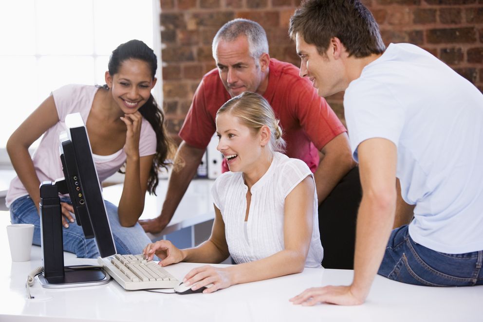 Zwei Frauen und 2 Männer sitzen vor einem Computerbildschirm am Tisch