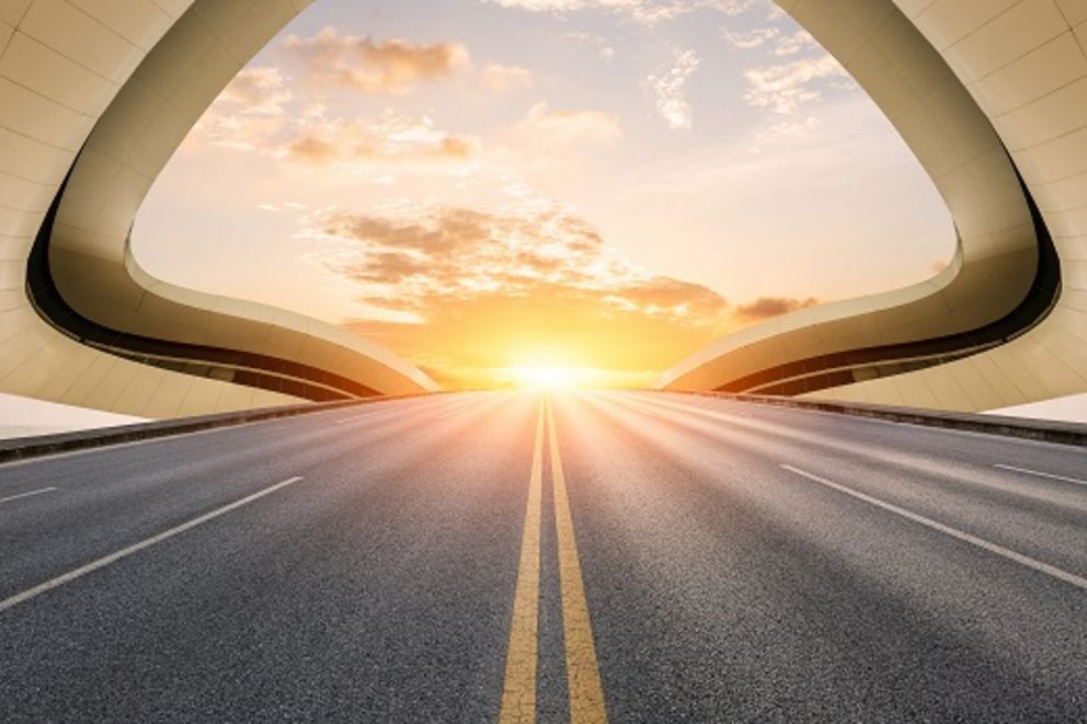 futuristisches Bild mit einer Straße, die aus einem geschwungenen Tunnel zum Sonnenaufgang führt